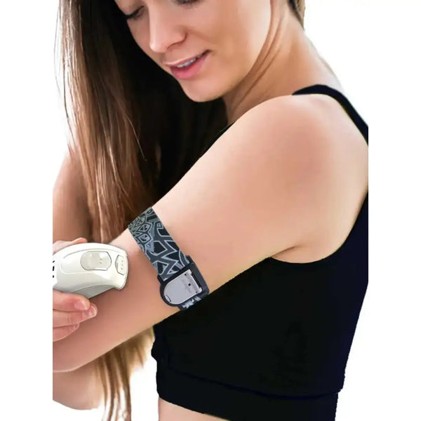 Woman wearing a patterned GlucoMen Day CGM adjustable armband on arm while holding glucose sensor device.
