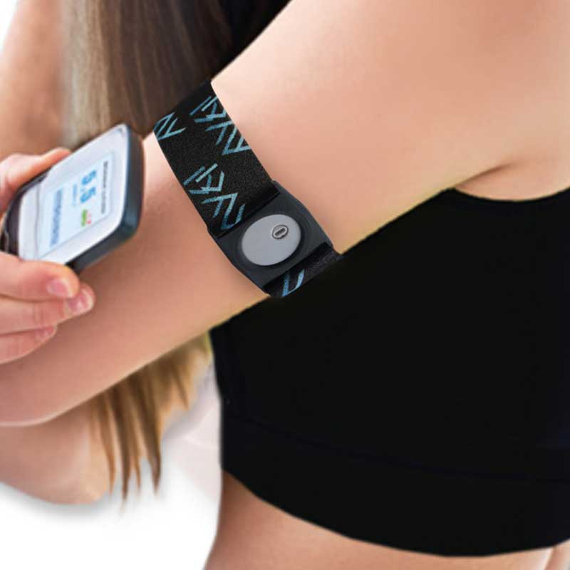 Person wearing a Freestyle Libre 3 armband on their upper arm, holding the glucose monitor to check levels. The black armband with blue patterns provides a snug fit for sports and activities. Immagine