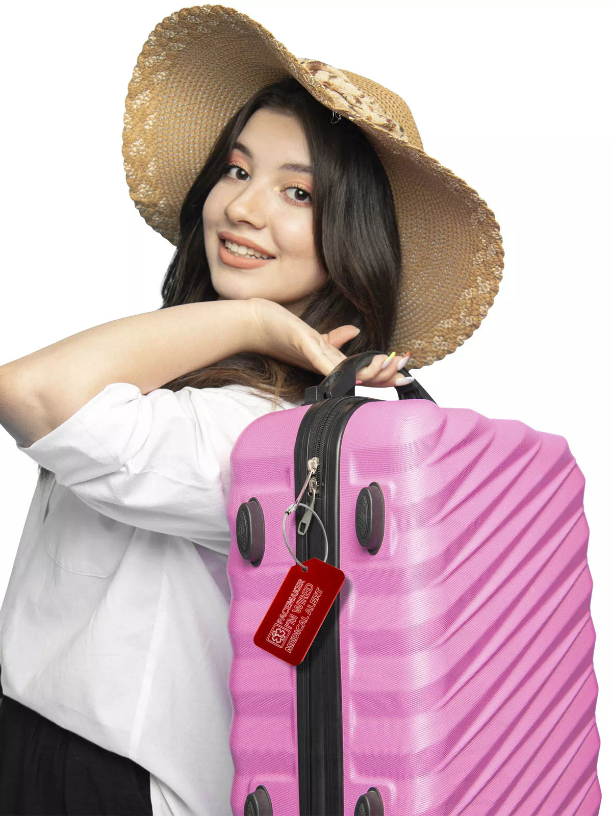 Woman wearing a hat and holding a pink suitcase with a red medical luggage tag attached.